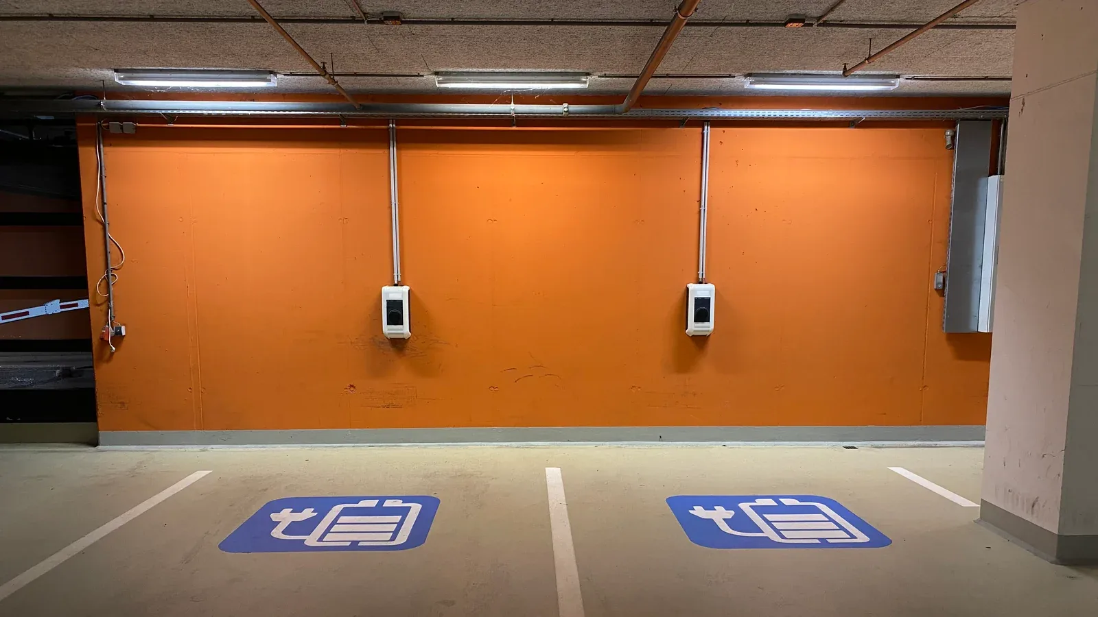 Deux bornes de recharge murales dans un parking couvert, devant des places signalées par des pictogrammes au sol.