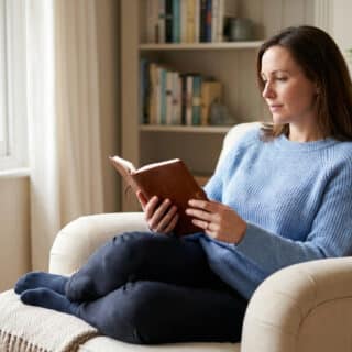 Une femme assise confortablement dans un fauteuil lisant un livre près d'une fenêtre.
