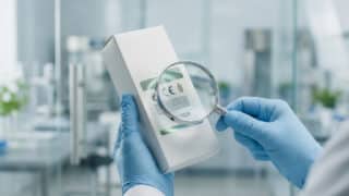 Mains gantées examinant l'étiquette d'un produit avec une loupe.
