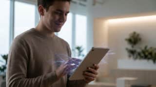Un jeune homme souriant utilise une tablette tactile avec des effets visuels de données numériques holographiques.