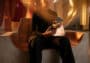 Une personne habillée en noir assise sur un siège moderne, tenant un smartphone affichant un fond d'écran abstrait doré.