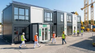 Ouvriers en tenue de sécurité marchant devant une base vie modulaire à deux étages sur un chantier.