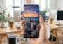 Main tenant un smartphone affichant une story Instagram au format vertical avec une vue sur une ville au coucher du soleil.