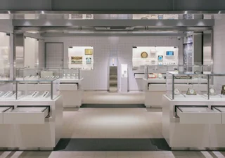 Vitrines en verre présentant des montres et des horloges, de part et d’autre d’une allée centrale